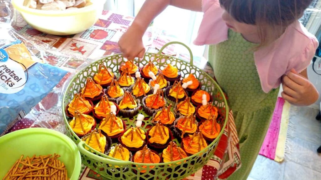 little girl putting marshmallow toothpicks onto cupcakes