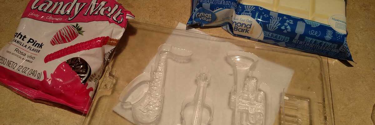 clear plastic mold for saxophone, violin, trumpet, and keyboard with pink candy melts and white almond bark in packages