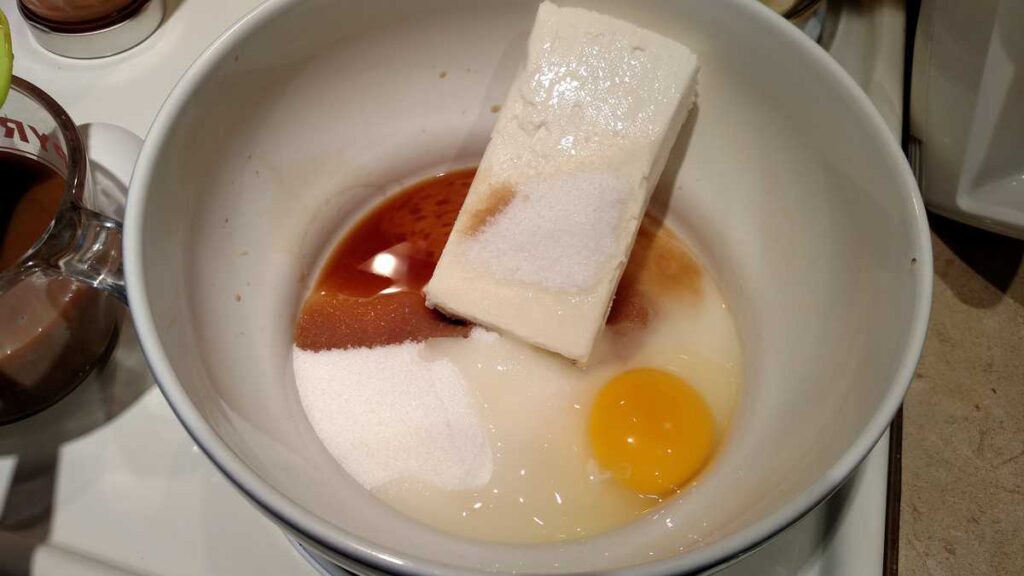 brick of cream cheese, sugar, egg, and vanilla unmixed in bowl