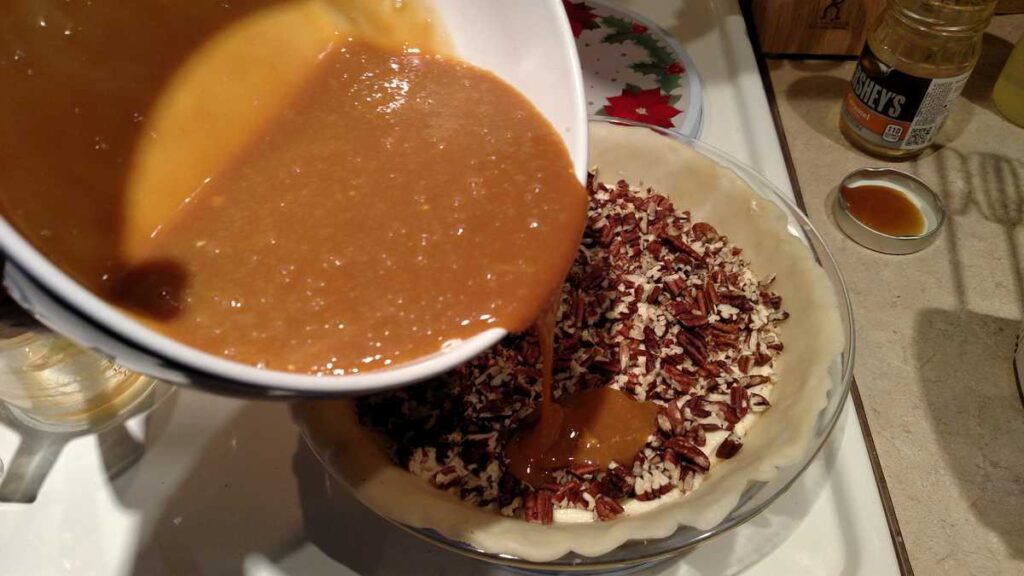 bowl pouring caramel sauce over nuts in pie