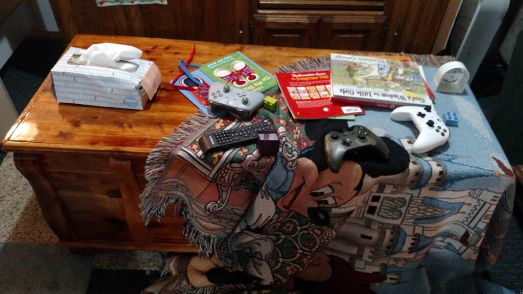 cedar chest with blanket, books, game controllers, tissue box, all disorganized and messy