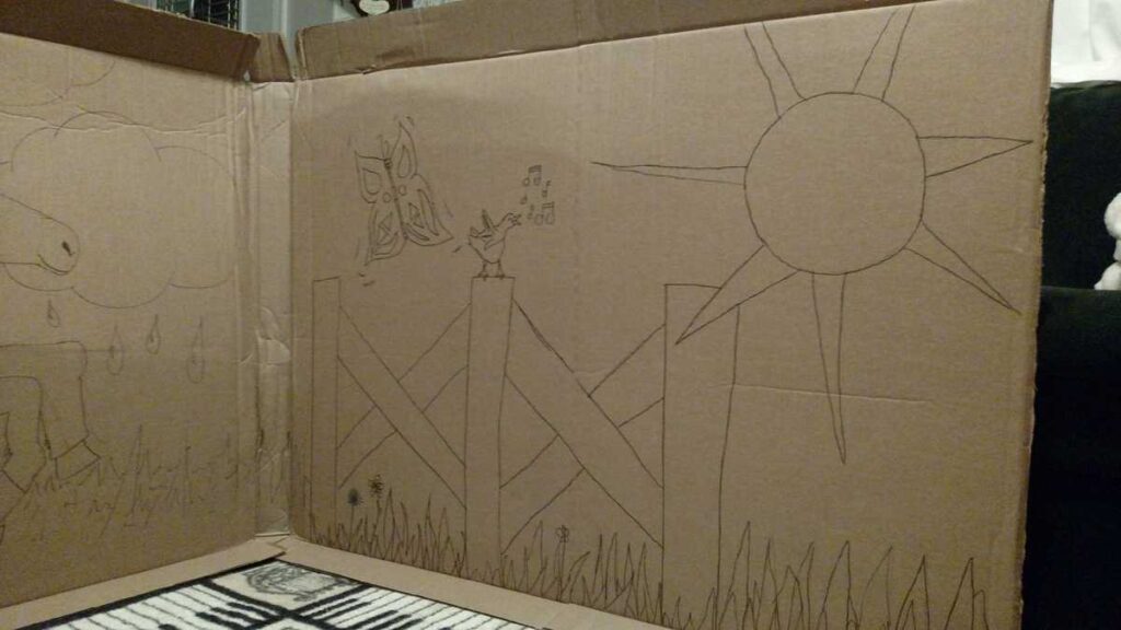 the fence side of an outdoor scene including the sun and butterflies, drawn on a large piece of cardboard