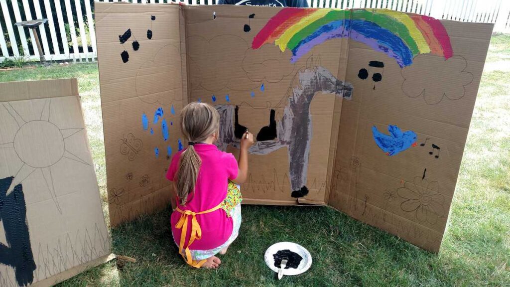 child painting large horse scene on a cardboard outdoors