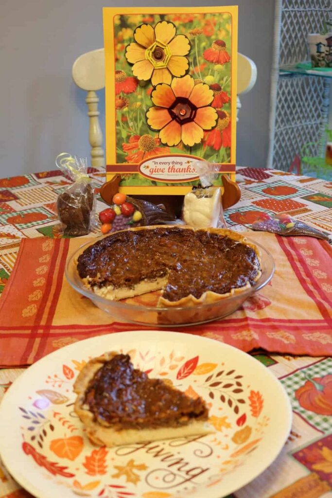 flower thanksgiving art in background, pie with piece cut out of it in middle, piece of pie on paper plate in foreground