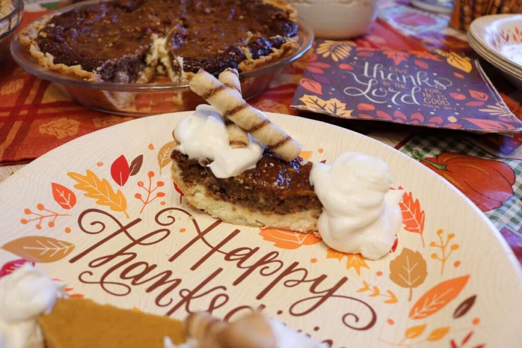 closeup of piece of pecan cheesecake pie with whip cream and wafer rolls on top, and whole pie in background