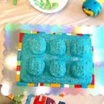 giant lego cake with blue frosting, surrounded by smaller legos bordering it