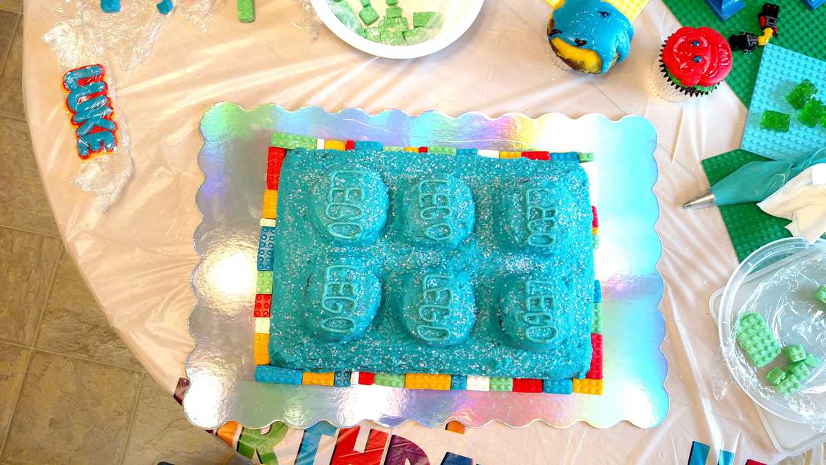 giant lego cake with blue frosting, surrounded by smaller legos bordering it