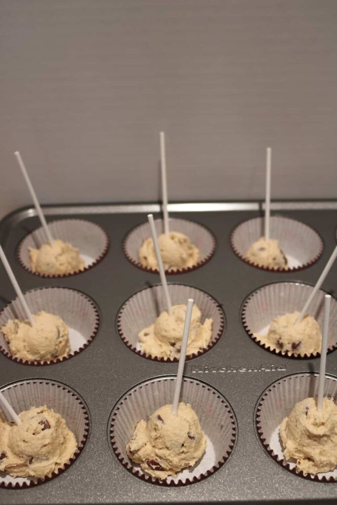 edible chocolate chip cookie dough in paper liners with lollipop sticks in them.