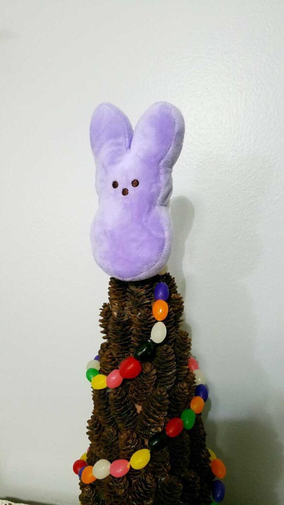 closeup of plush bunny Peep on a pine cone tree draped with a jelly bean garland