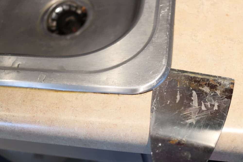 using a putty spatula to lift old sink off of kitchen counter