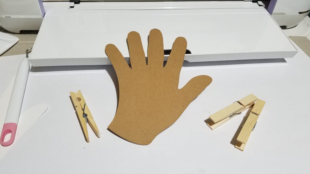 chipboard hand and clothespins in front of Cricut Maker