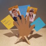 horizontal picture of cut out hand standing on countertop holding children's pictures and notes to dad