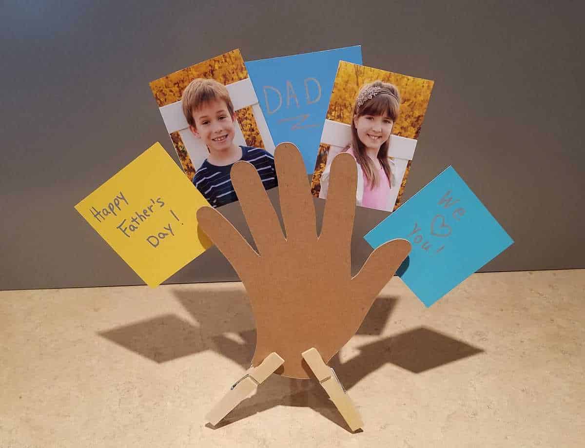 horizontal picture of cut out hand standing on countertop holding children's pictures and notes to dad