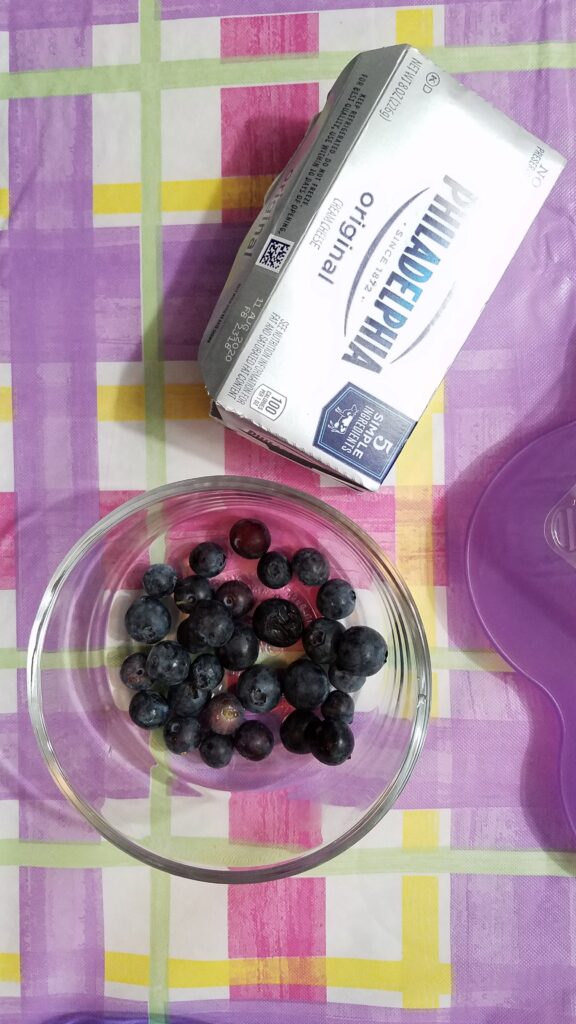 a box of Philadelphia Cream Cheese with some fresh blueberries in a clear glass bowl