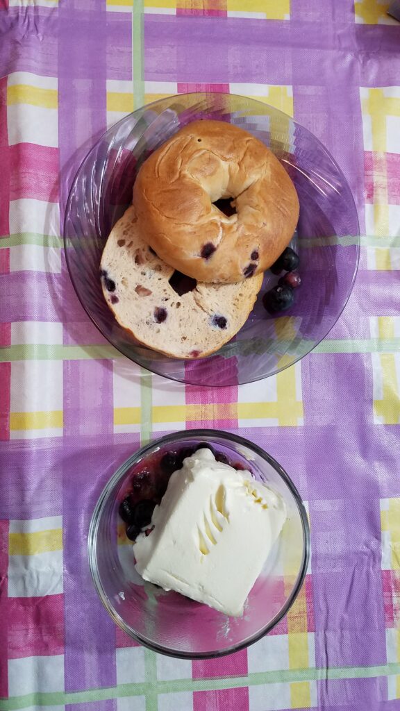 two slices blueberry bagel on a plate and cream cheese and blueberries in a bowl