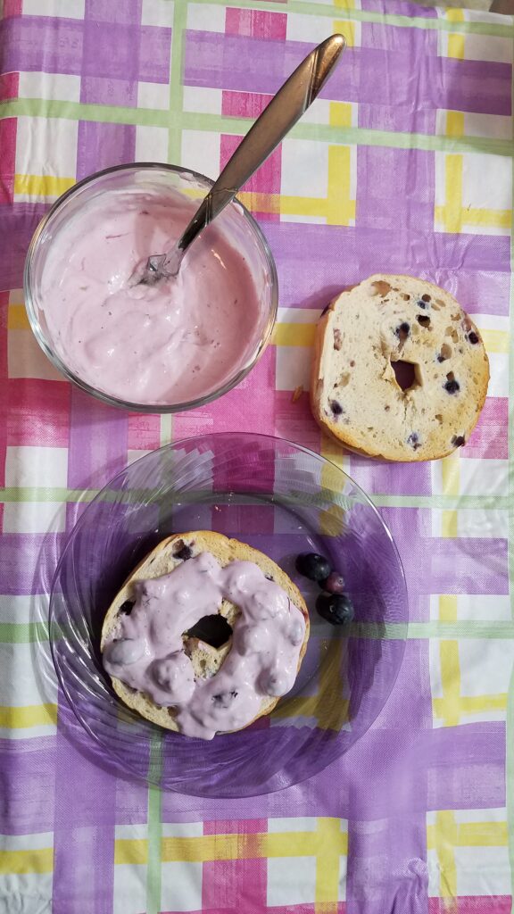 plain blueberry bagel slice, blueberry cream cheese on a bagel, and bowl of blueberry cream cheese