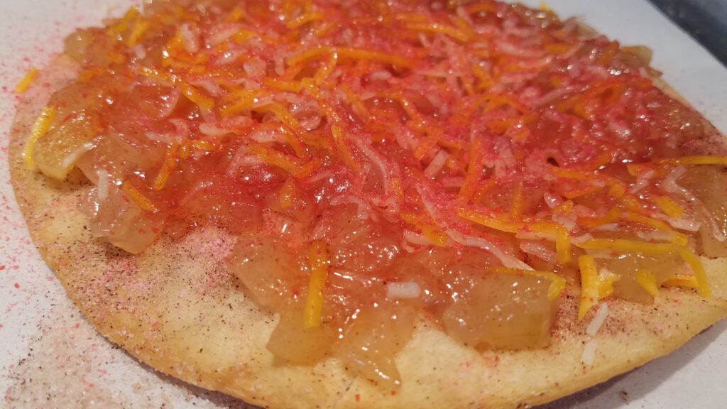 closeup of bright orange, hot pink color of red hots mixed with cheese on apple pie filling