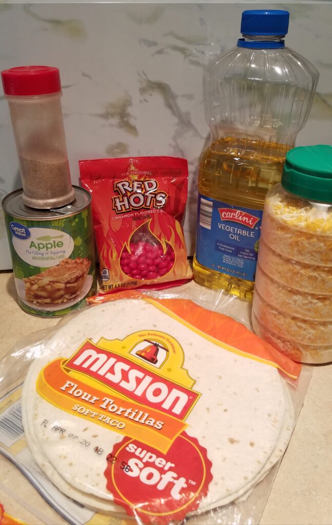 ingredients needed to make apple grande including flour tortillas, vegetable oil, shredded cheese, red hot candies, cinnamon sugar, and a can of apple pie filling