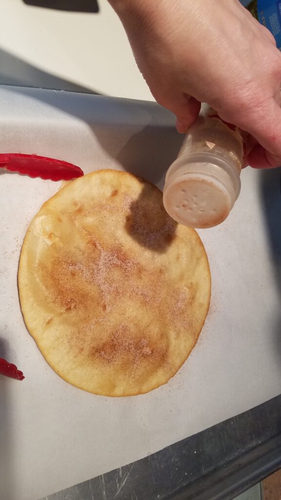 sprinkling cinnamon sugar on a fried flour tortilla