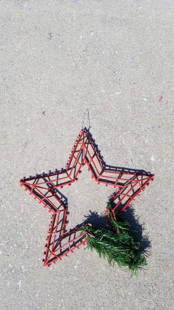 red plastic 5 point star shaped wreath form with some greenery on one corner