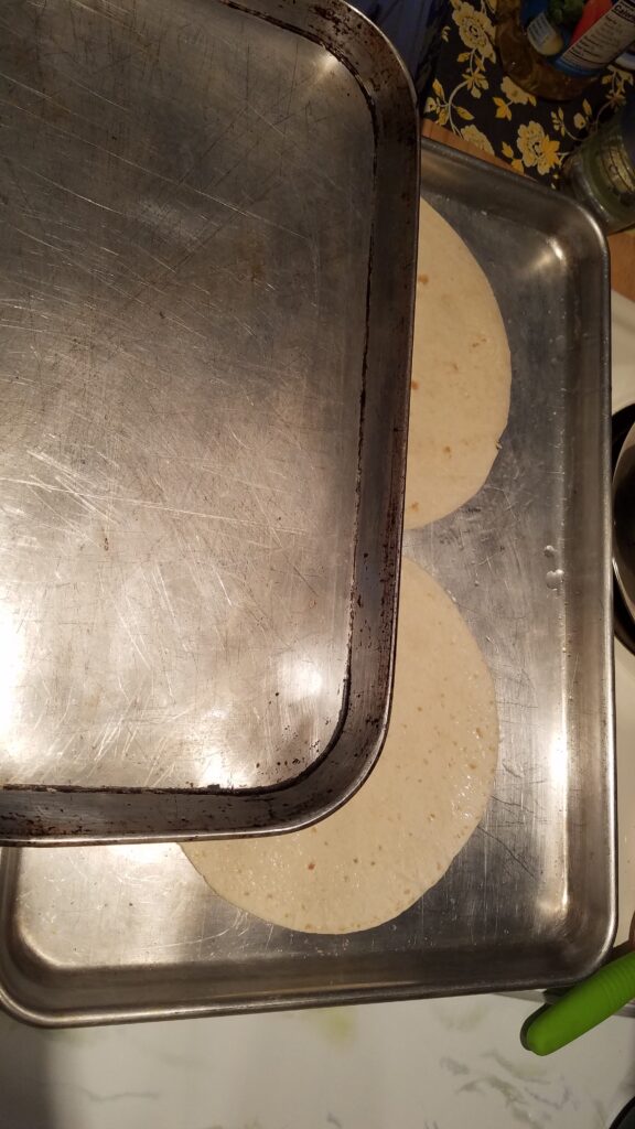 two flour tortillas on a cookie sheet with another cookie sheet partially covering them