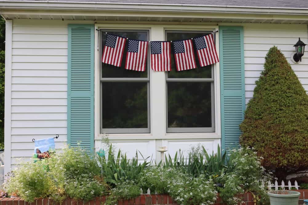 5 flags on banner in front of windows on house with green shutters