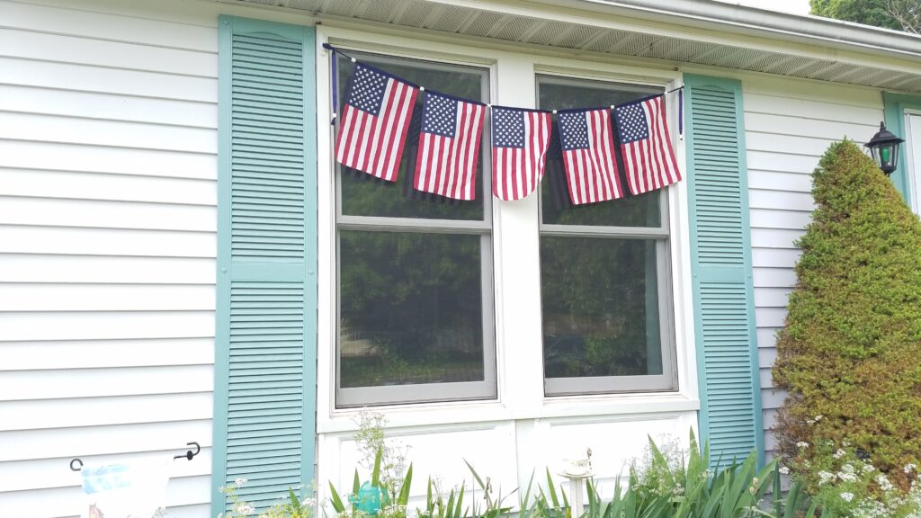 5 flags on banner in front of windows on house with green shutters