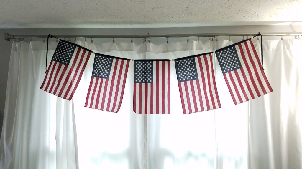 flag banner hanging inside house over white curtained windows