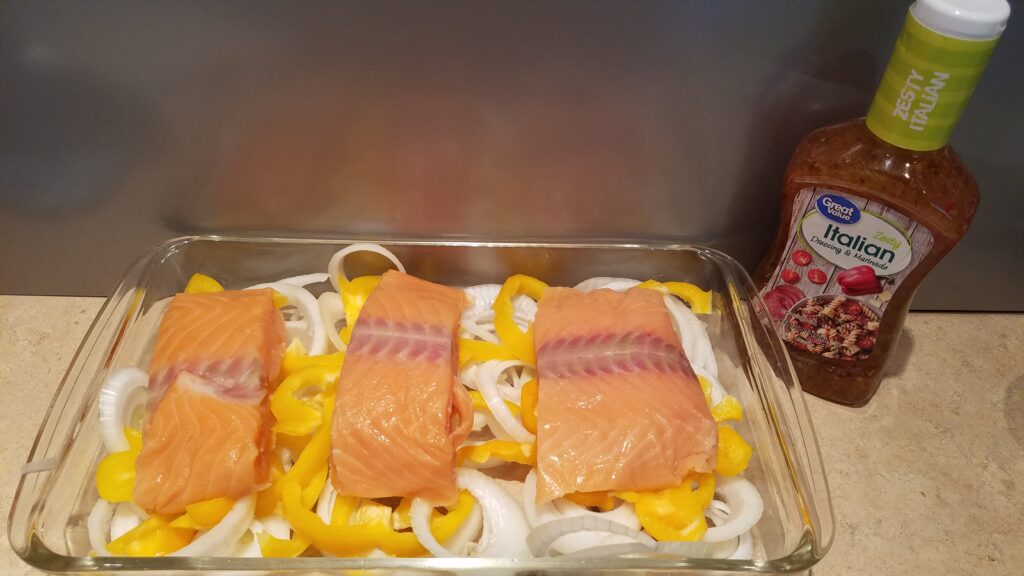 uncooked salmon, bell peppers, and onions, with a bottle of Italian salad dressing
