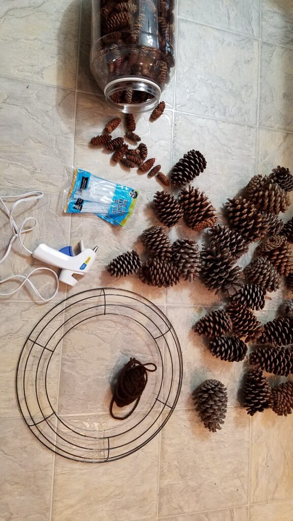 Pine cones, glue gun, glue sticks, wire wreath frame