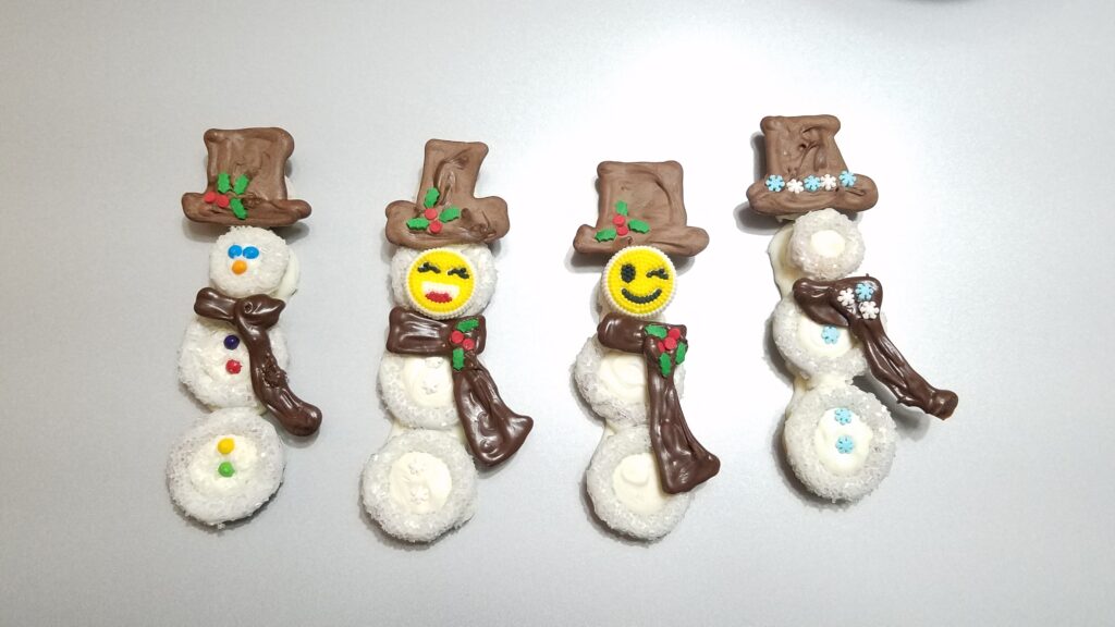 four pretzel snow people with chocolate scarves and hats