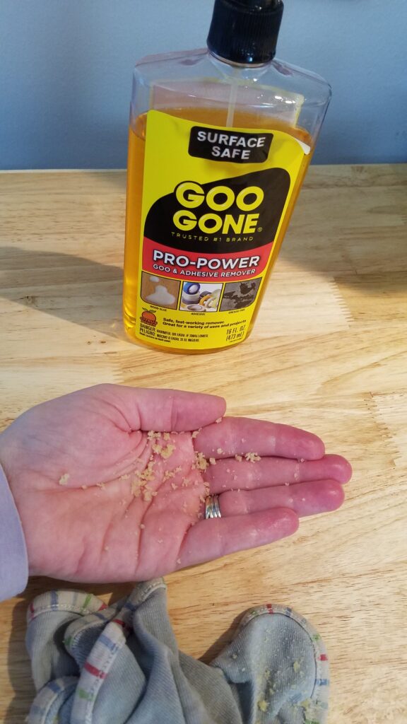 Goo Gone bottle with hand holding adhesive crumbs