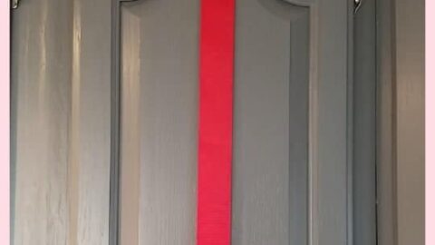 Joy to the World red paper plate on a red ribbon on a gray cabinet door