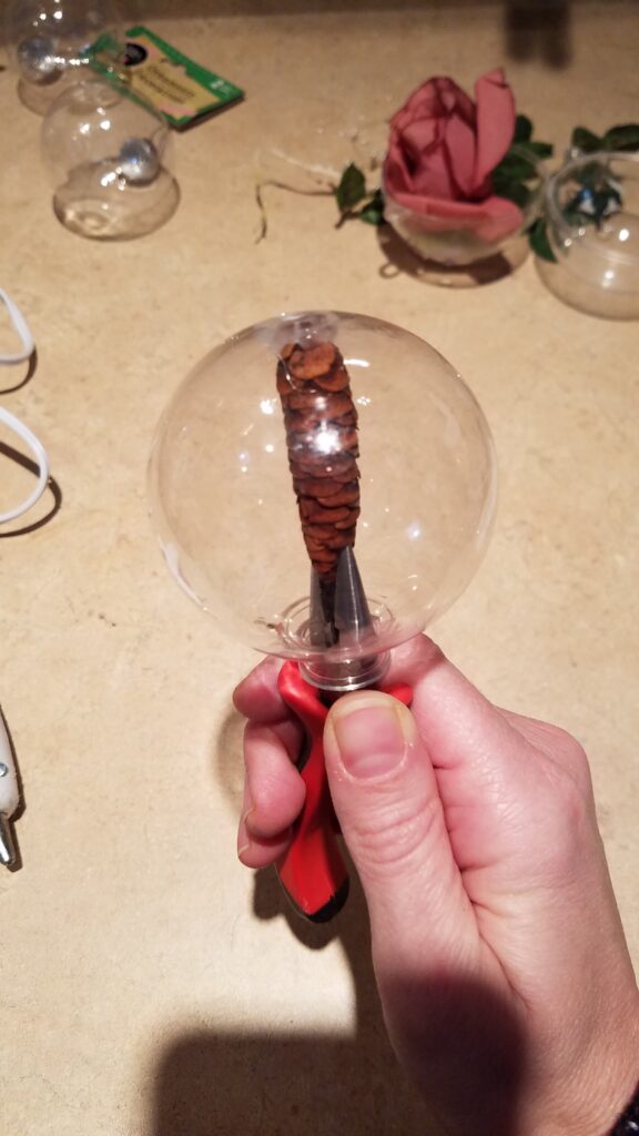 pine cone on a tweezer in a clear ornament