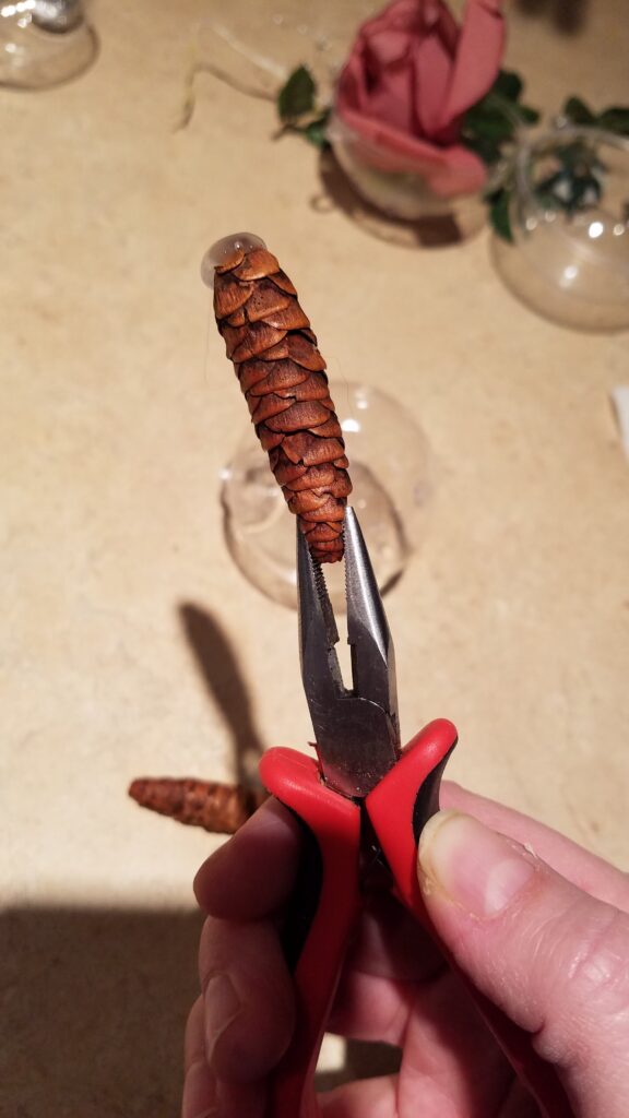 pliers holding pinecone with hot glue on the pine cone