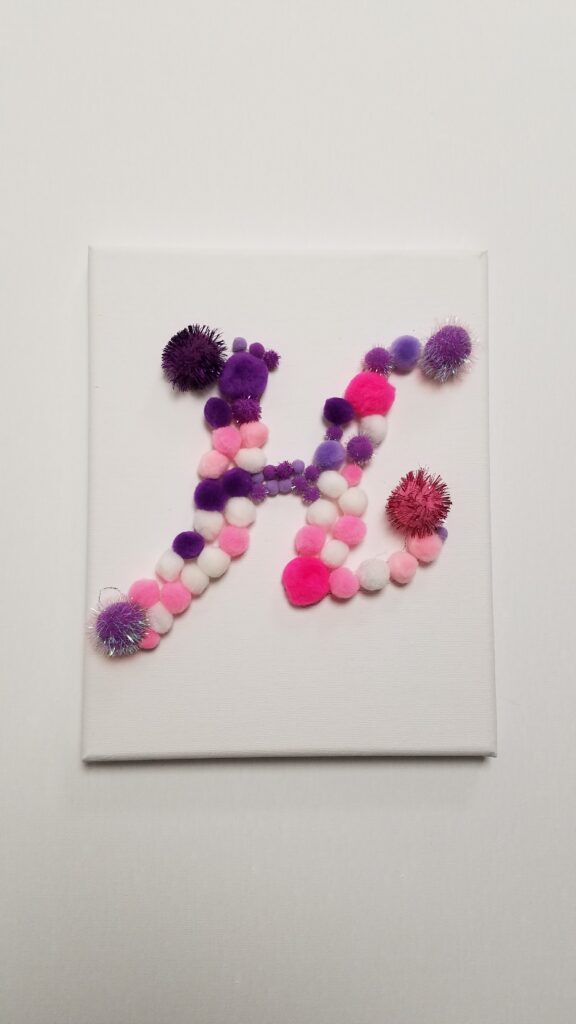 the letter H in pom poms on a white canvas