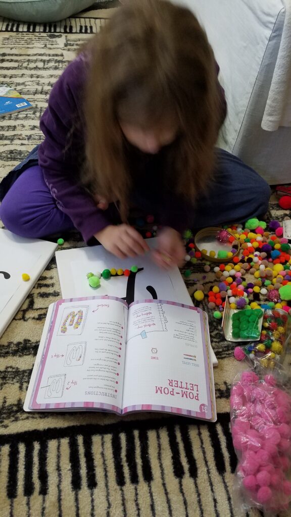 girl looking at book with pom poms beside her