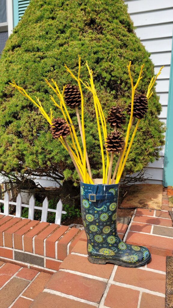 yellow painted dried stems and pine cones in a rain boot