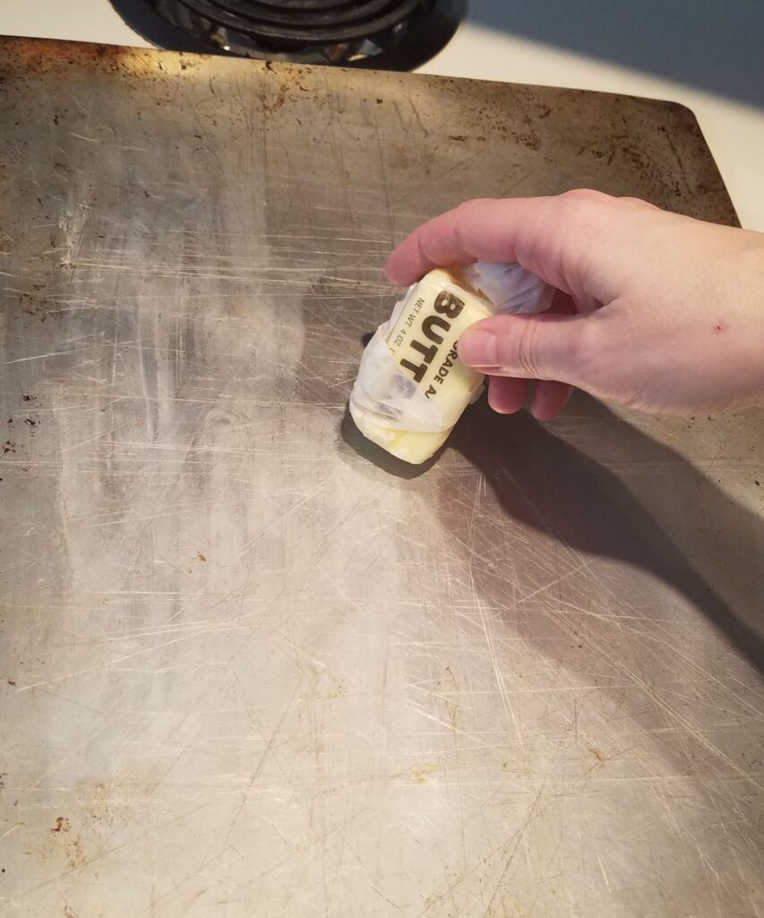 butter being spread on a baking sheet