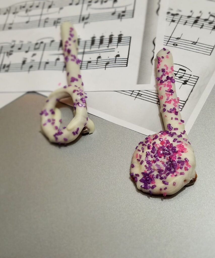 purple and pink sprinkles on a white chocolate covered music note pretzel