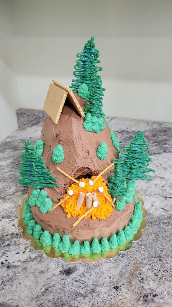 Colorful outdoor themed cake with trees, a tent, and campfire